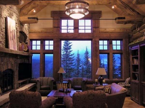 Cozy log cabin living room with large windows, stone fireplace, and warm ambient lighting.