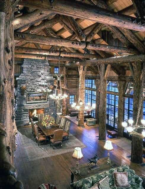 Grand log cabin interior with vaulted ceilings, stone fireplace, and rustic dining area.