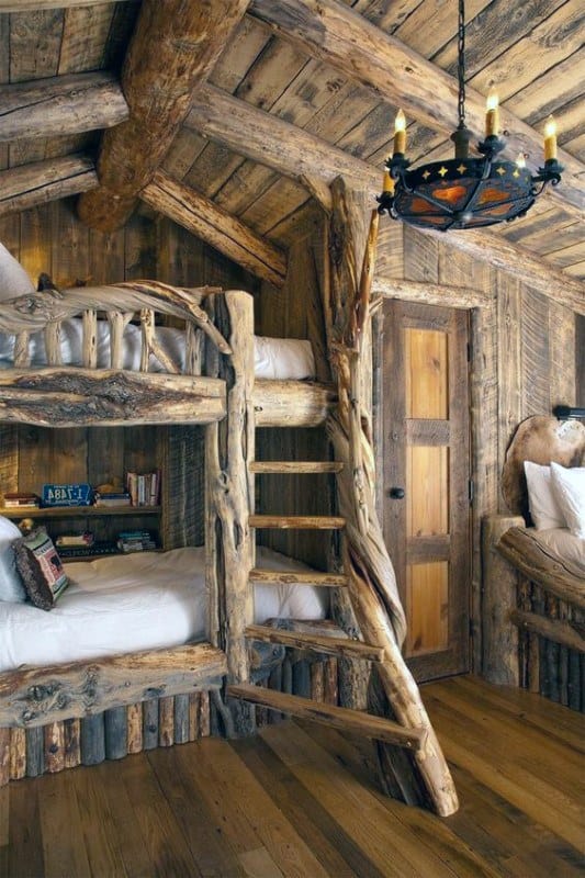 Charming rustic bedroom with handcrafted wooden bunk beds, a natural log ladder, and a warm chandelier for a cozy cabin feel.