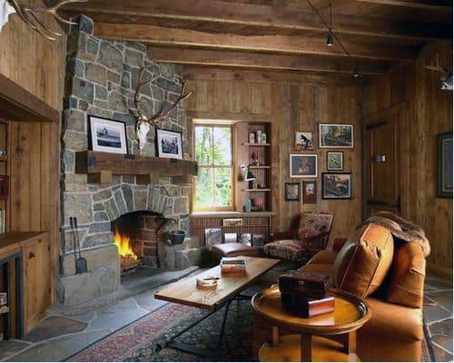 Log cabin living room with stone corner fireplace, leather armchair, patterned chair, and wood walls.