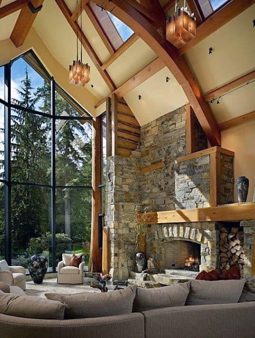 Rustic living room with a tall stone fireplace, exposed wood beams, and high vaulted ceilings.