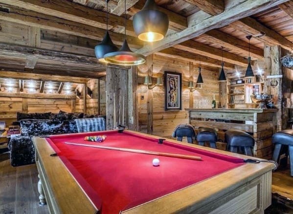 Rustic billiard room with red felt pool table, log cabin walls, and modern pendant lighting.