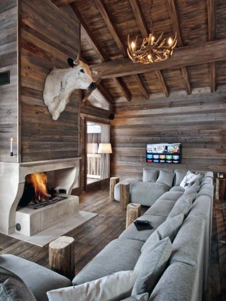 Rustic cabin living room with exposed wood beams, stone fireplace, and gray sectional sofa.
