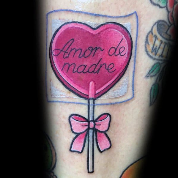 Heart-shaped pink lollipop tattoo with "Amor de madre" written on it, wrapped in clear packaging and tied with a delicate pink bow.