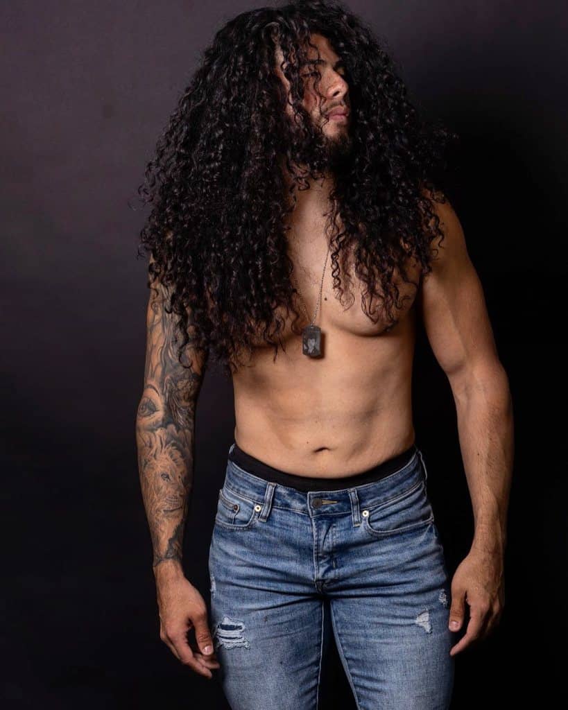 long bob men's hairstyle featuring long and close-packed curls. The curly hair covers forehead and cheeks