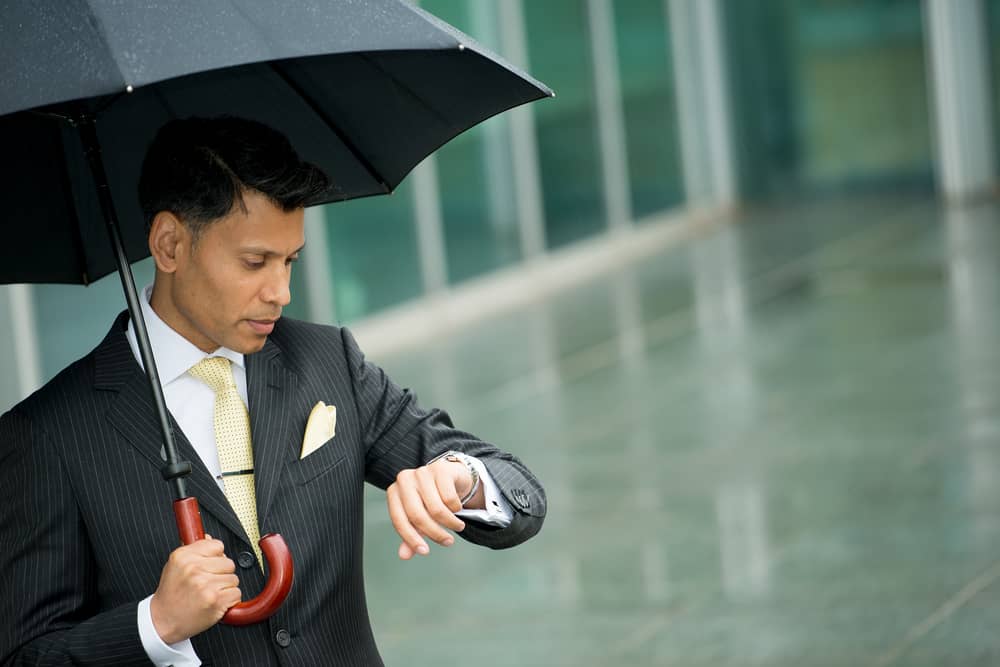 man in rain with umbrella looking time on his watch