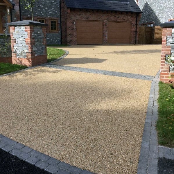 A resin-bound driveway with a smooth, golden gravel surface bordered by gray brick edging for a polished, modern appearance.