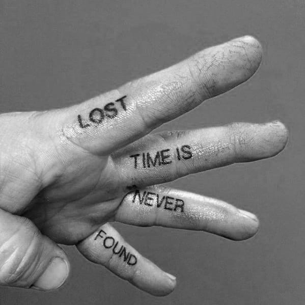 A hand with the words "LOST TIME IS NEVER FOUND" tattooed on the fingers