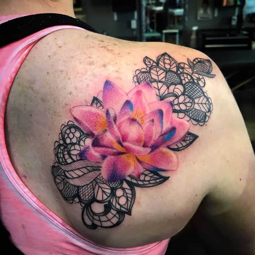 Shoulder tattoo featuring a vibrant pink and purple lotus flower with intricate black lace patterns and ornamental details.