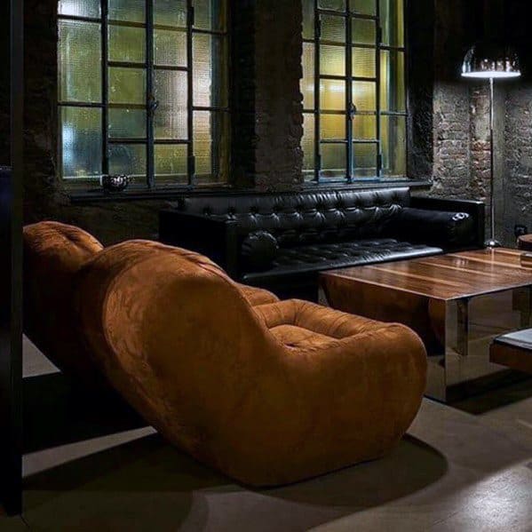 Brown suede lounge chair with black leather tufted sofa in an industrial-style living room.