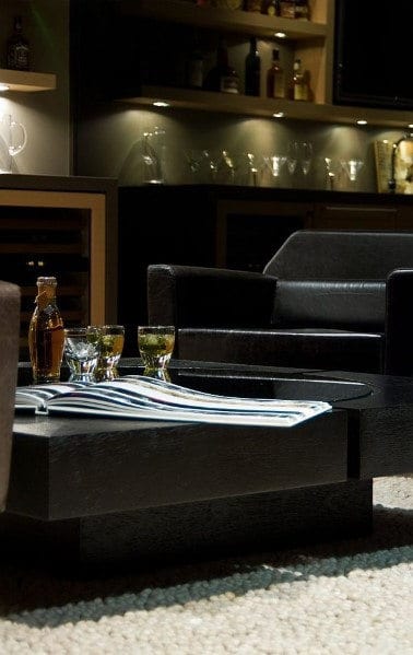 Modern lounge bar with black chairs, a table with whiskey glasses, bottles, and a book under soft ambient lighting