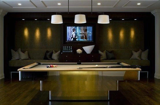 A dimly lit game room with a pool table, TV, and cushioned seating along the wall
