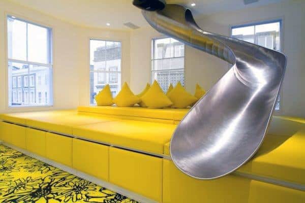 A bright room with a shiny slide and cozy yellow seating area with cushions