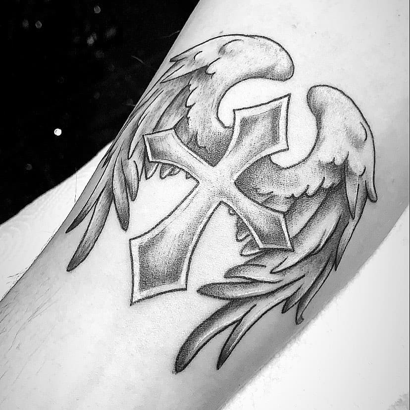 Tattoo of a cross with angel wings in black and gray ink