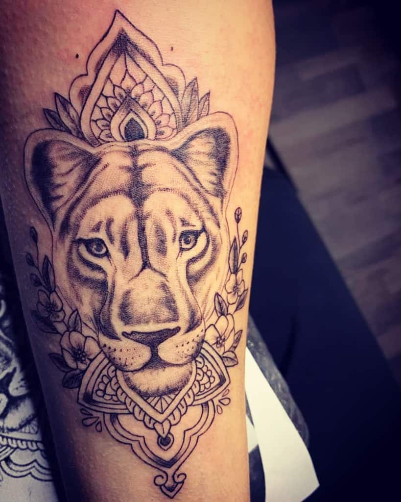 Intricate black and grey lioness tattoo on the forearm, featuring mandala patterns, floral elements, and fine shading for a regal and elegant look.