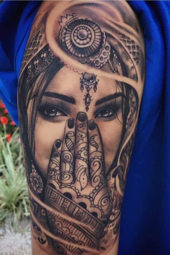 Hyper-realistic black and grey tattoo of a mysterious woman with intense eyes, ornate jewelry, and a henna-adorned hand covering her face.