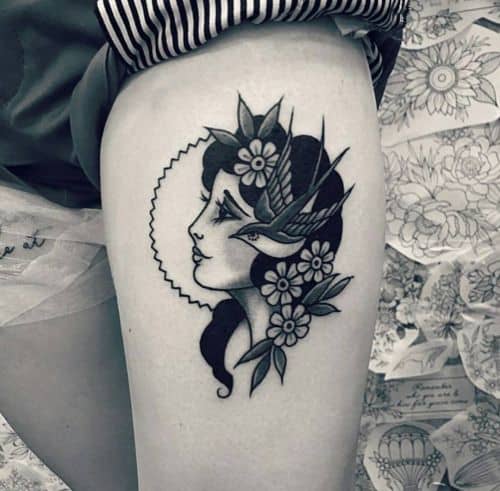 Black and grey tattoo of a gypsy woman with floral accents and a swallow bird, featuring delicate shading on the thigh.