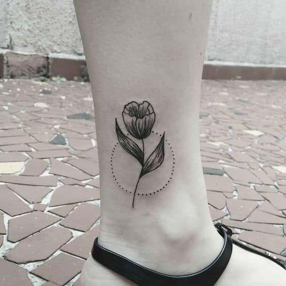 A minimalist tulip tattoo on the ankle with a dotted circle accent, featuring clean lines and soft shading for a delicate look.