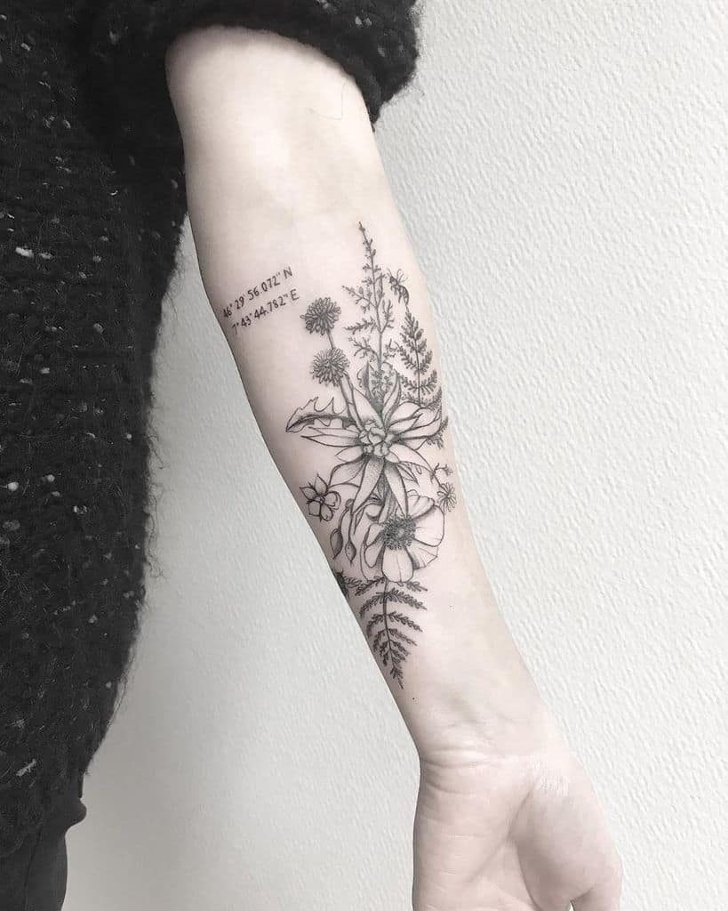 This tattoo combines detailed plants and flowers with geographical coordinates, adding a personal touch.