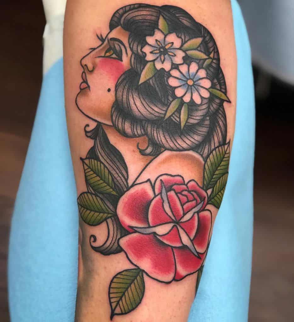 Traditional tattoo of a gypsy woman with floral hair ornaments and a large red rose on the forearm.