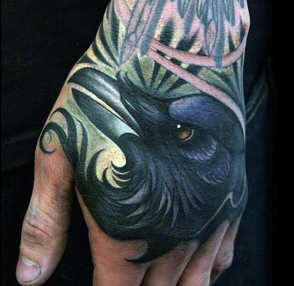 A detailed, colorful raven tattoo on a hand with intricate shading and design