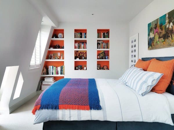 Modern attic bedroom featuring white and orange shelves, artwork on the wall, and blue/orange bedding