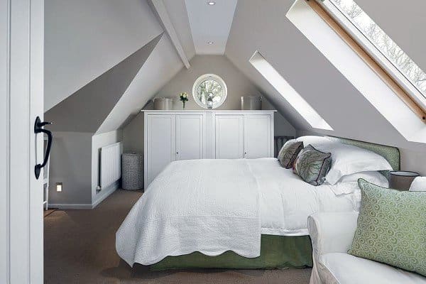 Cozy attic bedroom featuring a sloped ceiling, white bedding, and skylights above a small round wardrobe window