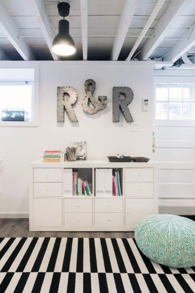 Modern basement with exposed beams, white decor, and a striped rug for a cozy look.