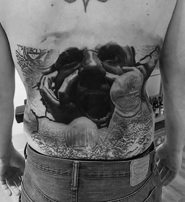 Black and grey tattoo of a person’s face emerging from cracks in the skin, with intense facial expression and detailed shading, creating a dramatic and surreal effect.