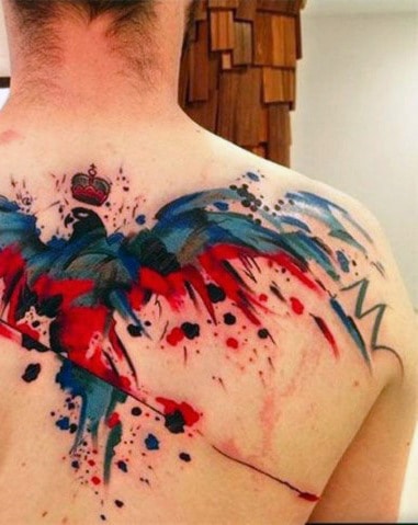 Abstract tattoo on a person's upper back with splashes of red, blue, and black