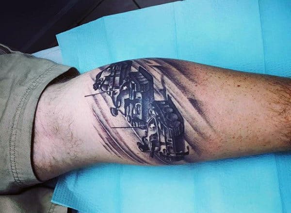 Black and grey calf tattoo of military armored vehicles moving through a desert landscape, with dynamic shading for a realistic effect
