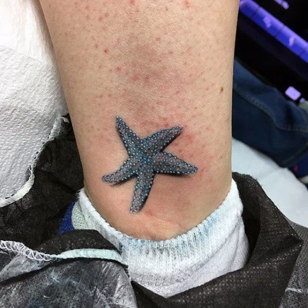 Small blue starfish tattoo on the inner ankle with fine dot texture and realistic shading, placed just above the sock line.