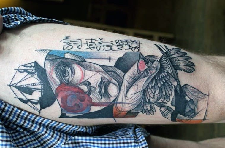 Abstract tattoo of a man's face with geometric shapes and text on a person's arm