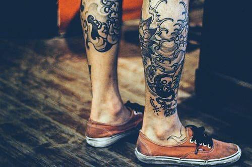 Lower leg tattoos with Japanese-style designs featuring waves and traditional figures