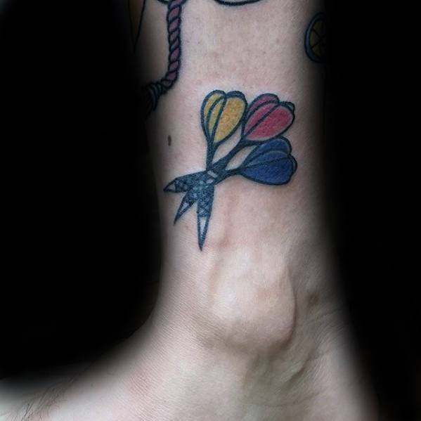 Colorful ankle tattoo of three darts in blue, red, and yellow with a bold outline, combining a playful and classic style.