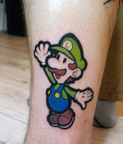 Tattoo of Baby Luigi in a cheerful pose with bold outlines and bright colors, inked on the lower leg in a classic cartoon style.