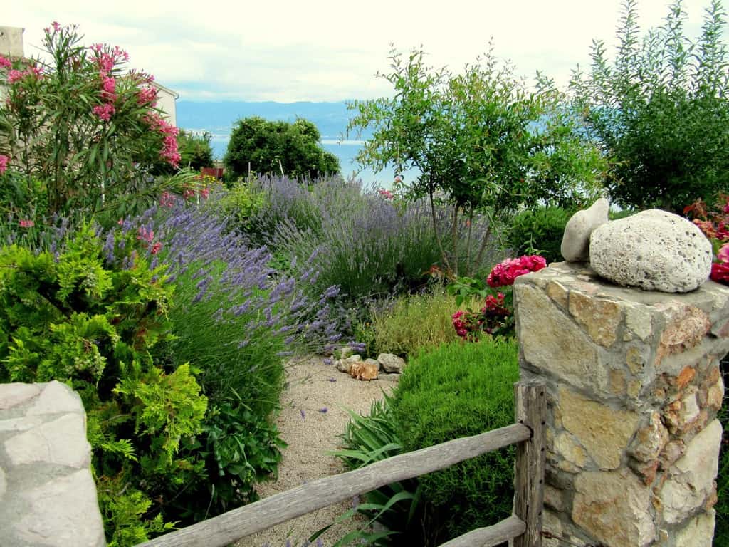 lush flower garden stone fence post wood gate sea view