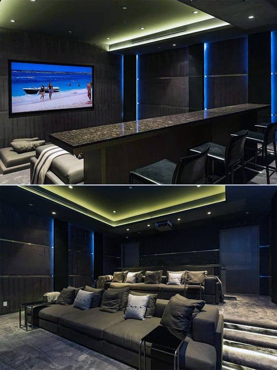 Luxurious home theater featuring a large screen, bar seating, and tiered sofas in cozy dim lighting