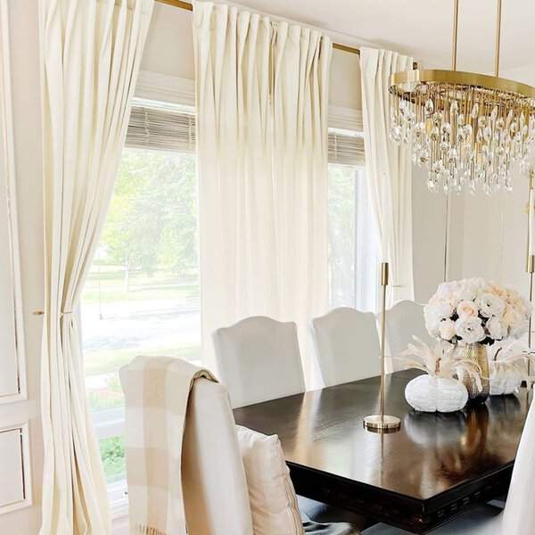 Elegant dining room with floor-length white curtains, a crystal chandelier, and a dark wood table.