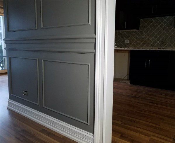 Gray wall with decorative molding, white baseboards, and hardwood floors.