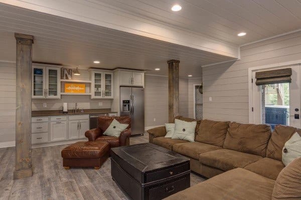 Cozy basement living room with sectional sofa, kitchen area, and recessed lighting.