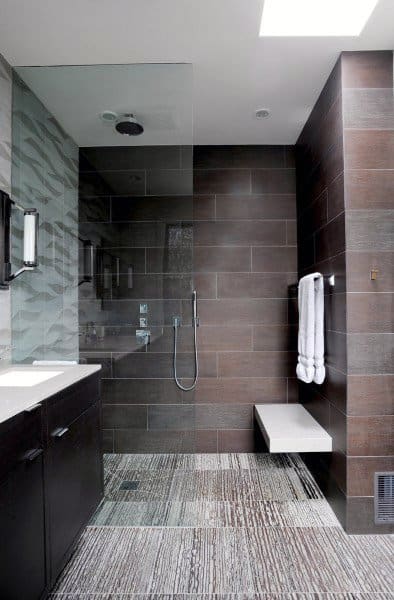 Modern bathroom with a spacious walk-in shower, brown tiled walls, a bench, and light streaming through a skylight