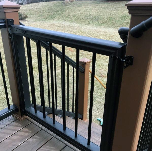 A black metal gate graces the wooden deck, with lush grass beyond