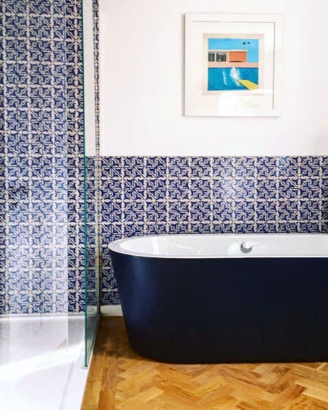 Blue freestanding bathtub with patterned blue tiles and wooden flooring.