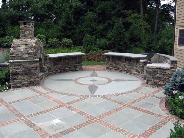 Brick patio with stone fireplace, circular design, and built-in benches surrounded by trees