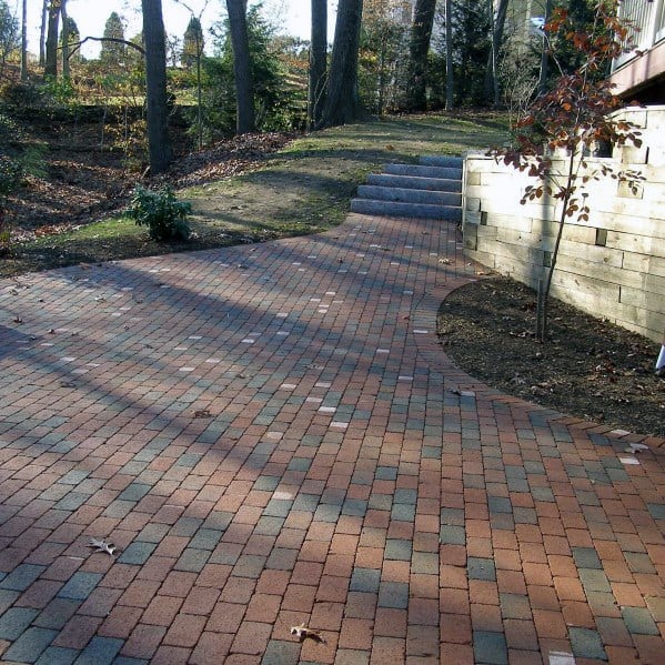 Brick walkway guides toward outdoor steps amid trees and a brick retaining wall