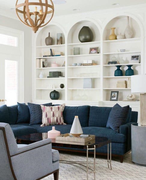 Elegant living room with arched white built-in bookcases, navy sectional sofa, and a modern wooden chandelier