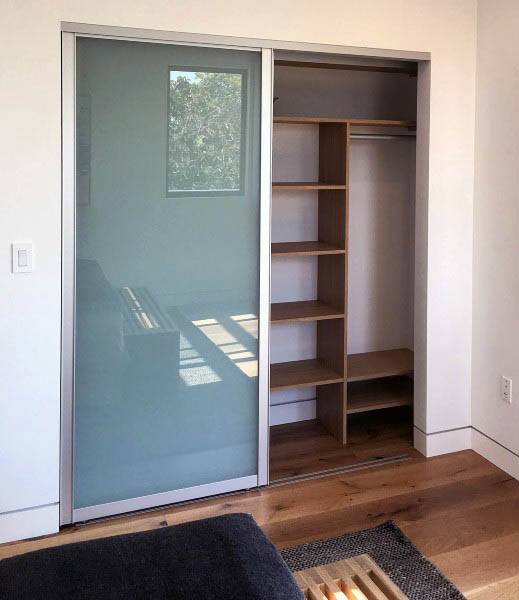A room with a closet's sliding door open to reveal shelves and hanging space on a wooden floor