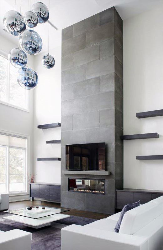 Tall concrete fireplace with modern shelving, glass firebox, and reflective pendant lights.