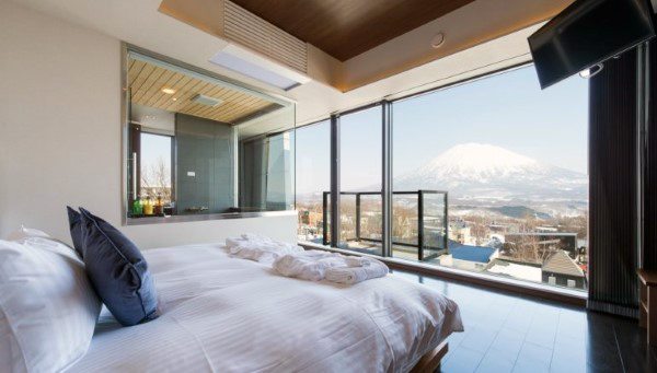 Modern minimalist bedroom with mountain views, glass walls, and an open ensuite bathroom.